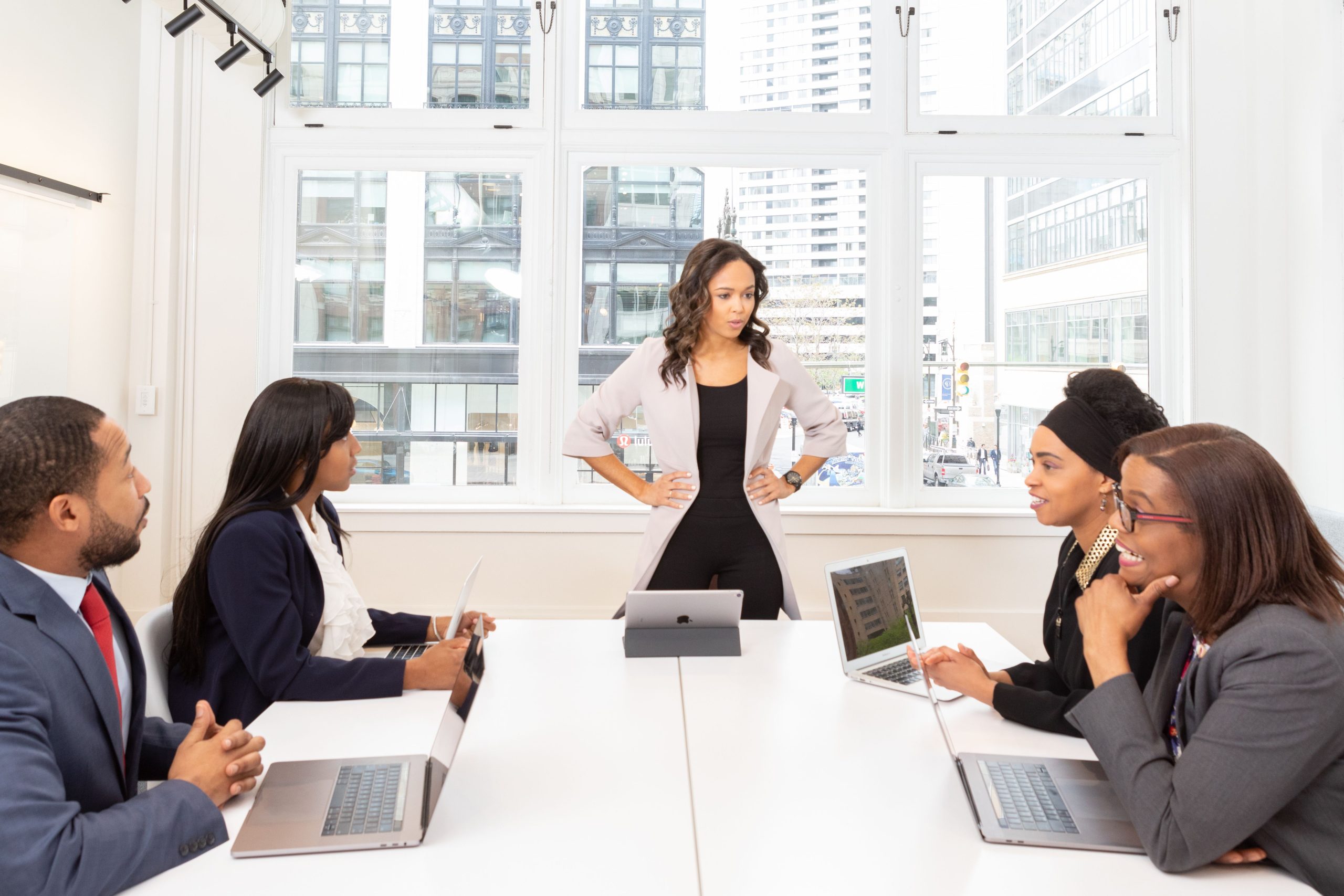 Assertiveness & Confidence Skills A diverse group of professionals engaged in a meeting at a modern office with laptops and city view.