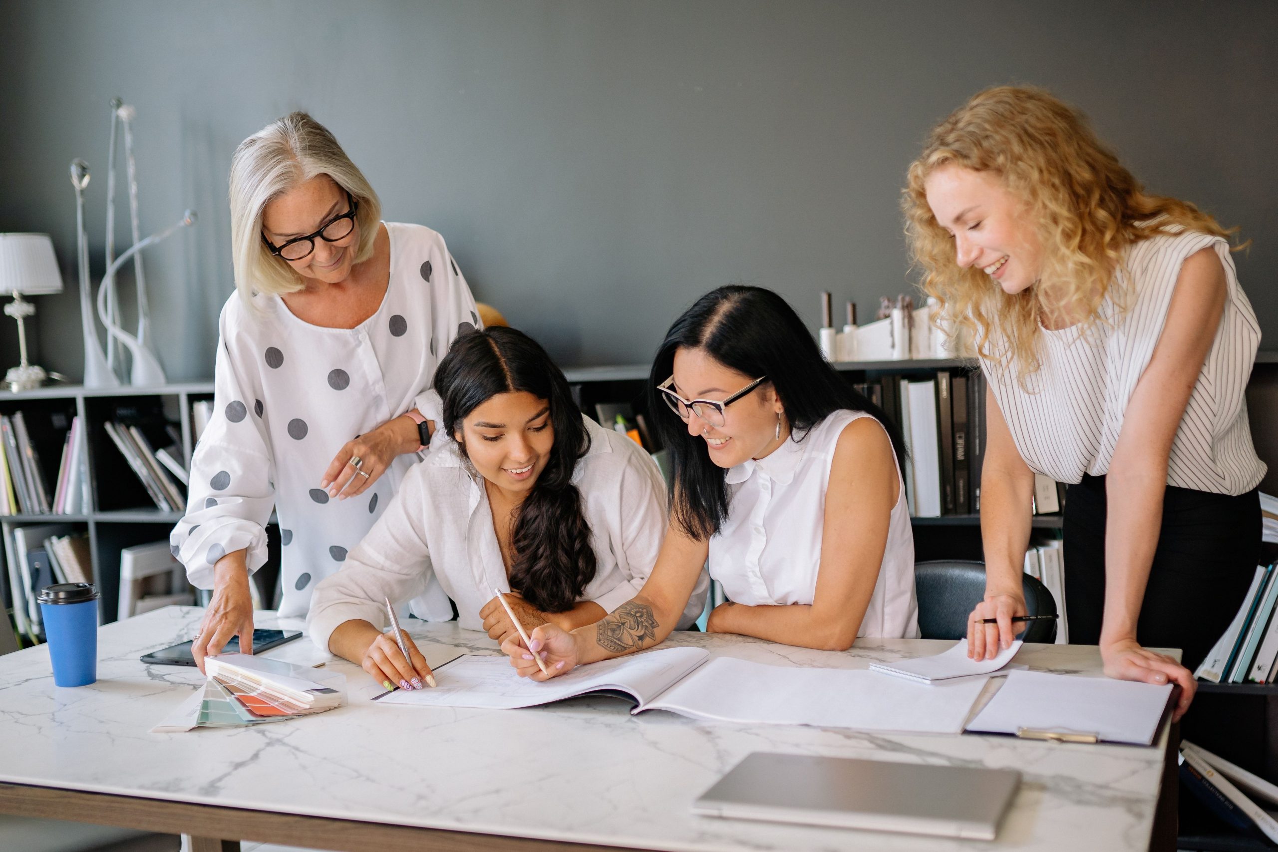 Project Management Course (PRINCE2) Four diverse women brainstorming ideas in a modern office environment with enthusiasm.